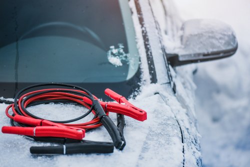 Jumper cables rest on the hood of a snow covered car.