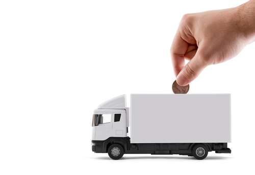 A hand drops a coin in a truck shaped piggy bank.
