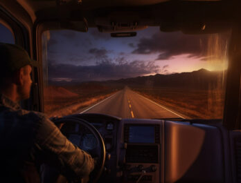 truck driver in his truck cabin driving down an empty road towards some mountains at dusk